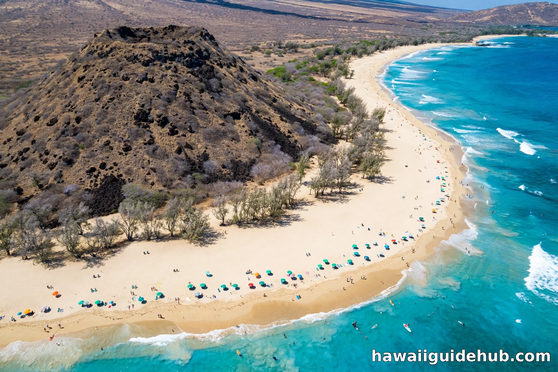 Aerial view of Big Beach (Oneloa) at Makena State Park, Maui, with golden sand, turquoise water, beachgoers, and the Puu Olai cinder cone