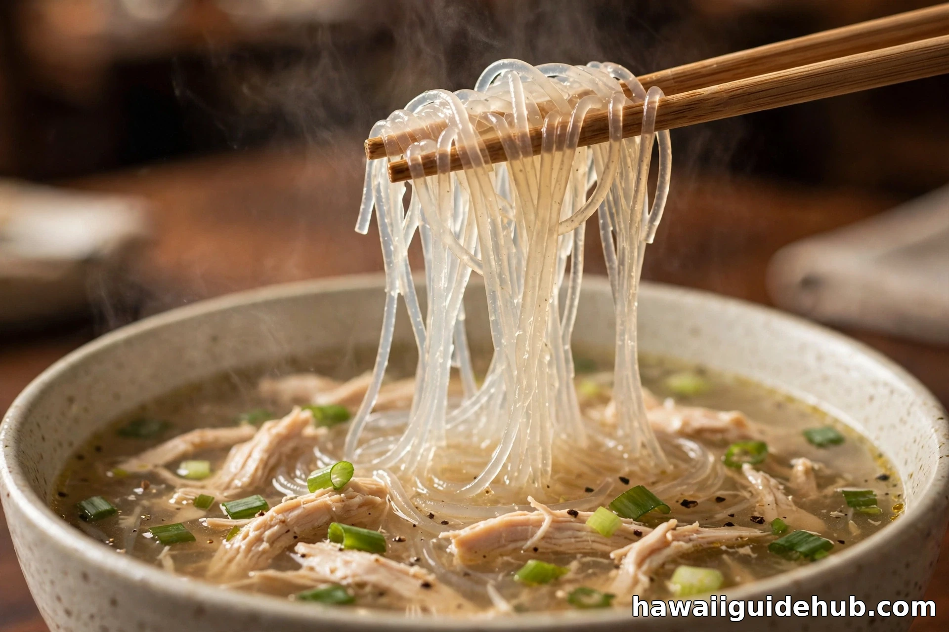 Chopsticks lifting translucent long rice glass noodles from a steaming bowl of Hawaiian chicken long rice soup