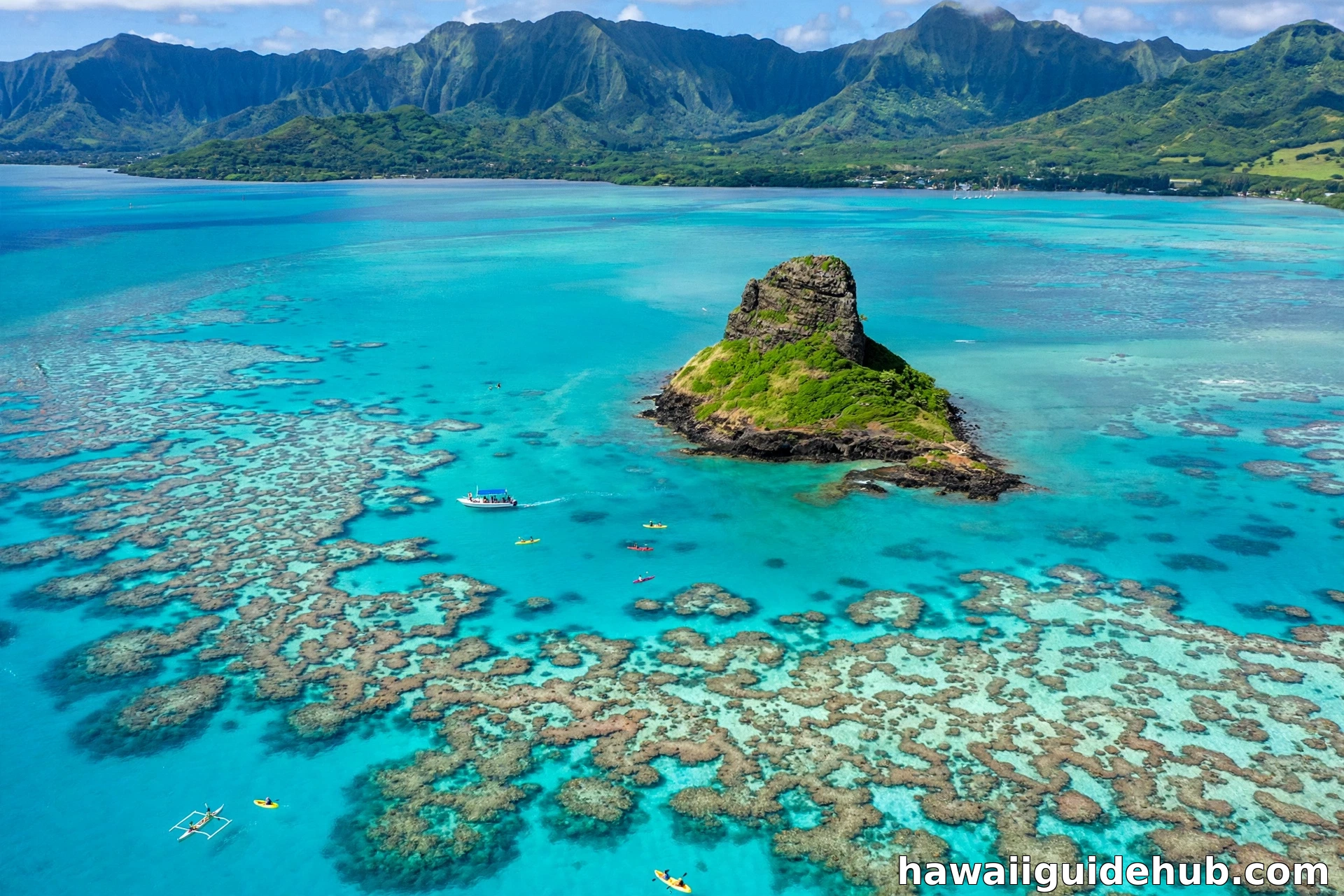 Aerial view of Kaneohe Bay with turquoise water, coral reefs, kayakers, and Mokoli'i island rising from the bay