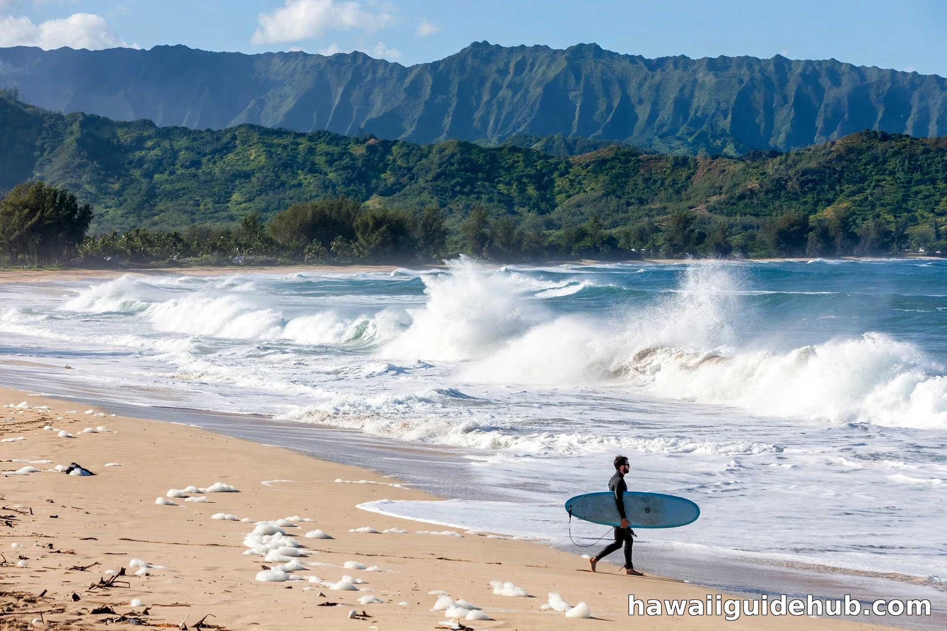 Surfer walking along Kekaha Beach as waves break with green Kauai mountains in the background