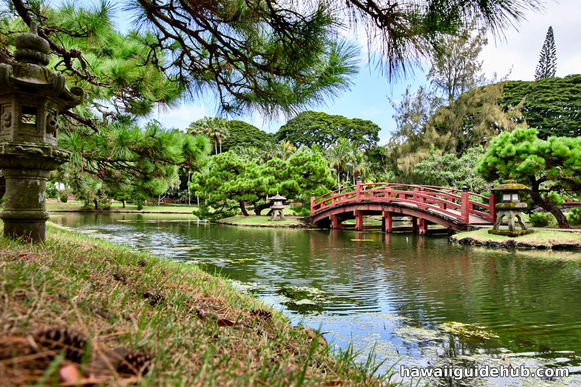 Liliuokalani Gardens on the Hilo waterfront with a red arched bridge over a pond, palm trees, and the harbor visible across Hilo Bay