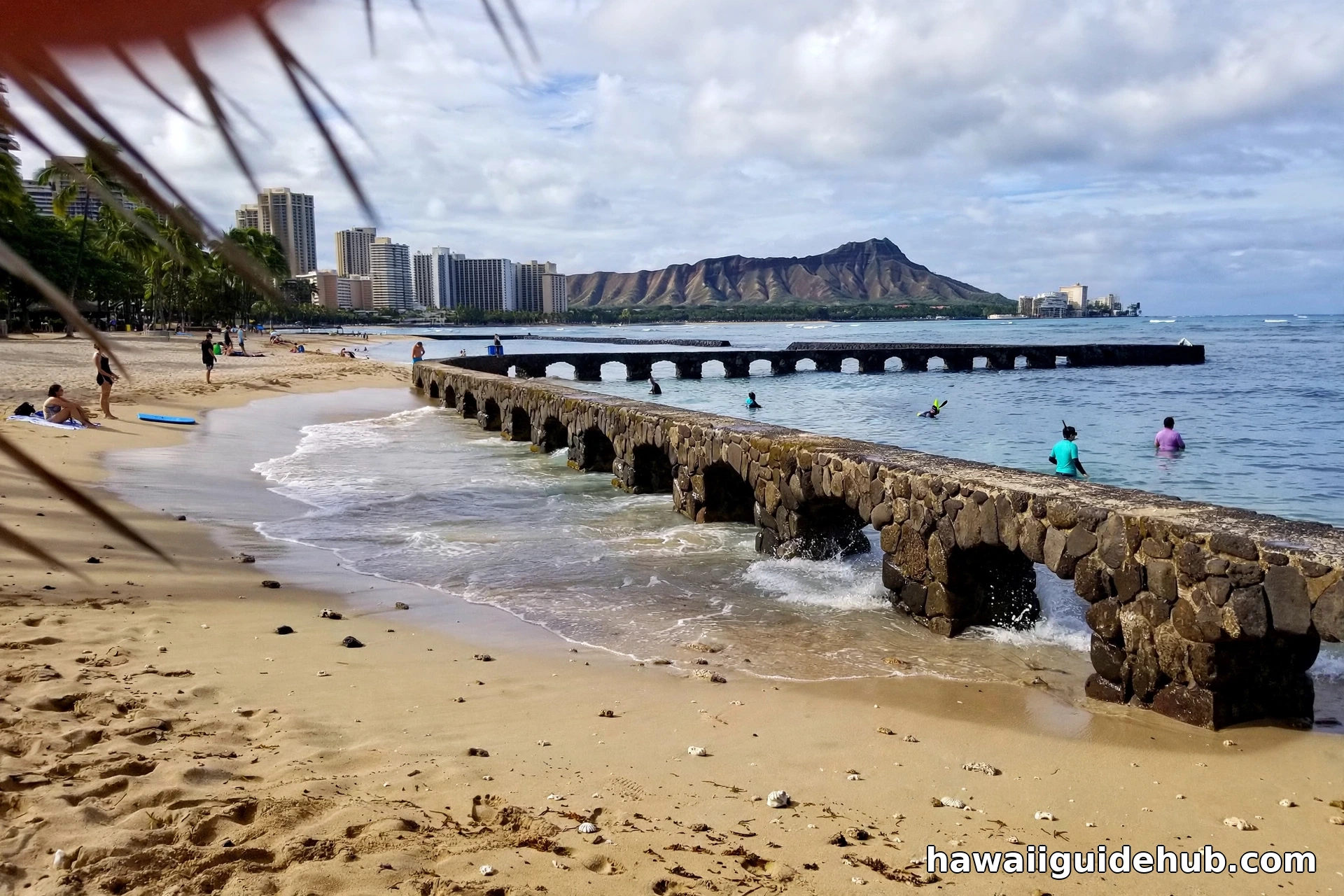 Families wading in the calm sheltered Ponds at Kuhio Beach Park with the Duke Kahanamoku statue nearby in Waikiki