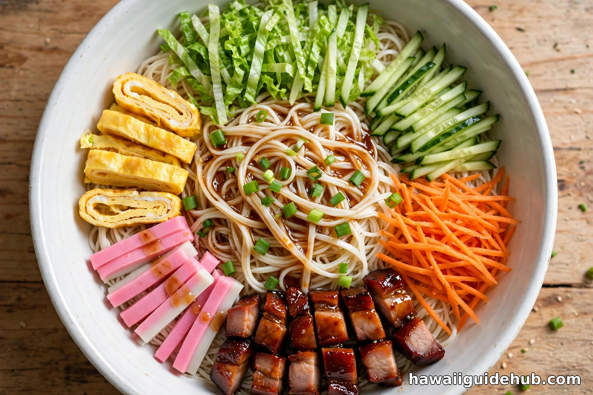 Overhead view of Hawaiian somen salad in a white bowl with noodles, kamaboko, egg, char siu, cucumber, carrots and lettuce