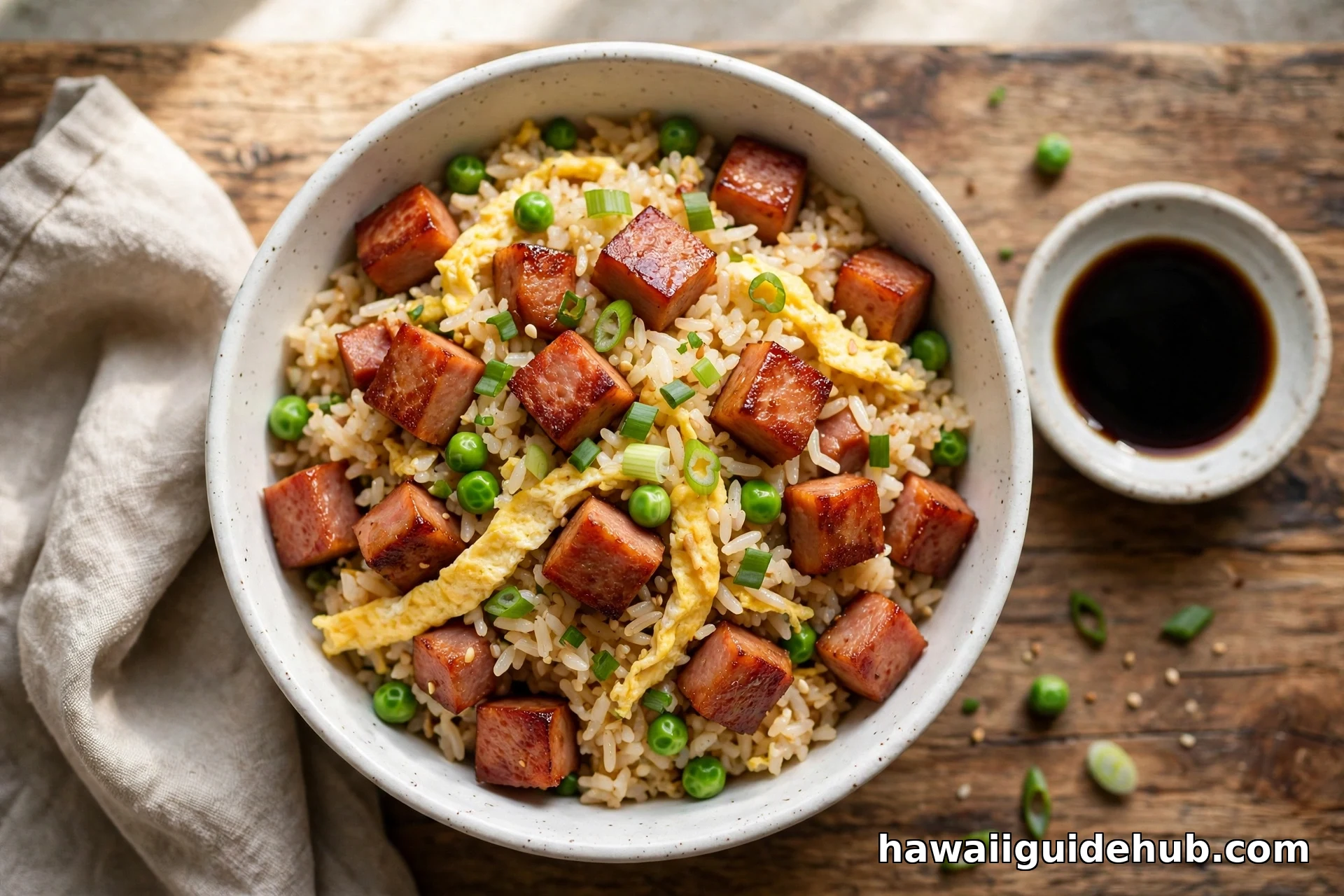 Bowl of Hawaiian spam fried rice with crispy SPAM cubes, egg ribbons, green onions, and peas on a wooden table