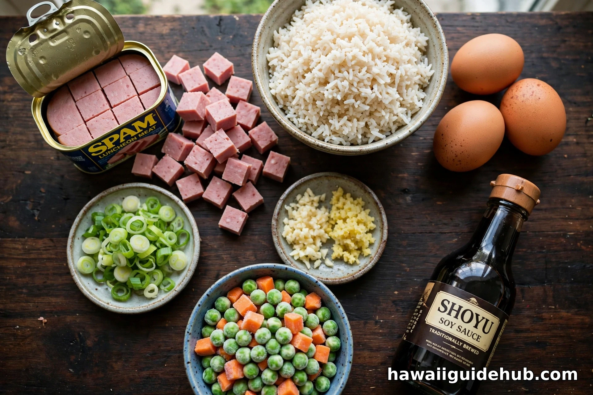Flat lay of spam fried rice ingredients including SPAM can, rice, eggs, green onions, garlic, peas, carrots, and shoyu