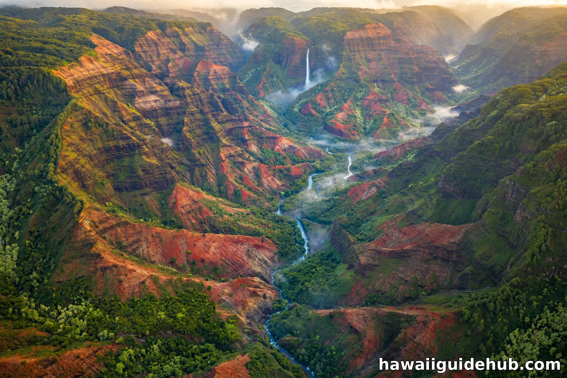 Aerial view of Waimea Canyon on Kauai with red cliffs, a waterfall, and morning mist